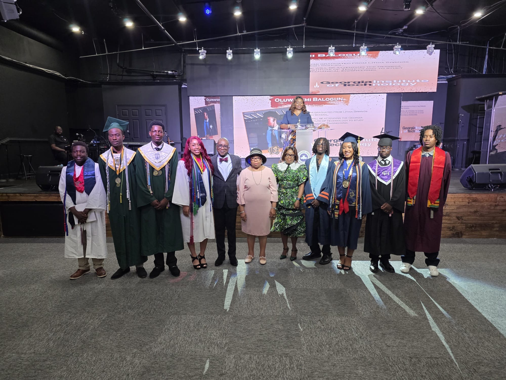 This picture features the latest high school graduates in their graduation attire. They are accompanied by Pastor and his wife and Mrs. Kemi, who is the leader of the children's ministry at t